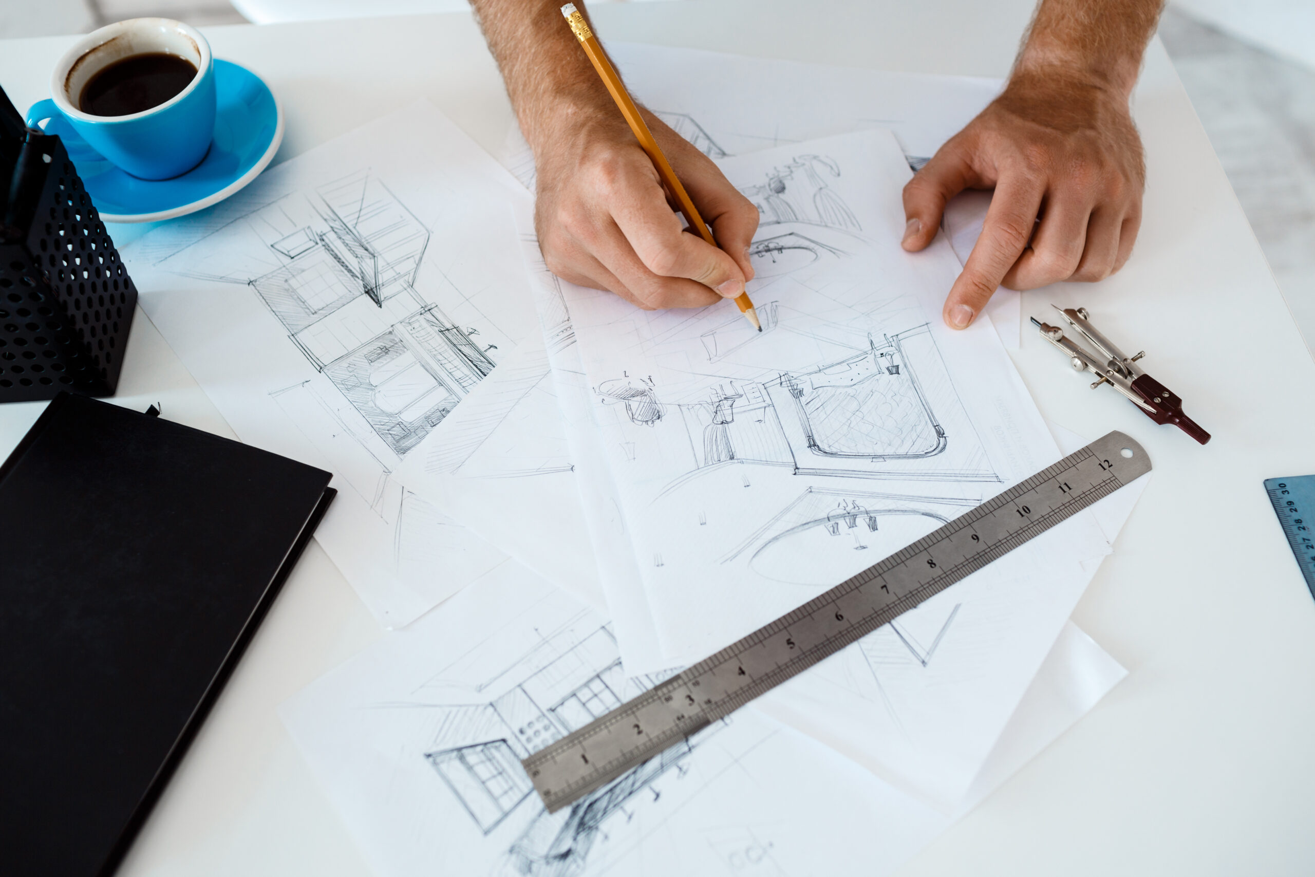 Hands of young businessman holding pencil and drawing sketch at table. White modern office interior background.